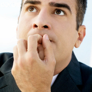 Worried businessman outdoors with finger in mouth, extreme close-up